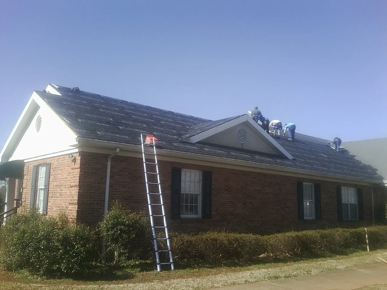 Crew tearing shingles off a brick ranch roof with a ladder set — Emergency Roof Repair work by our crew in Greensburg
